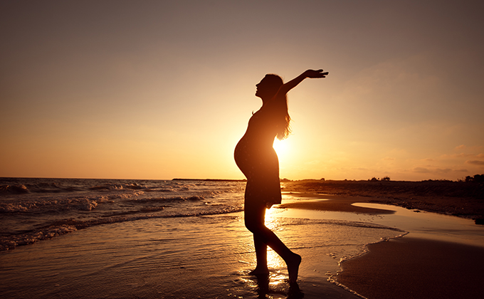 silhouette of a pregnant woman walking on the beach at sunset