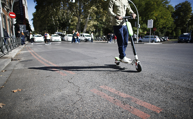 Un patinete pasa cerca de una línea naranja que indica restricción al tráfico en el centro de Madrid