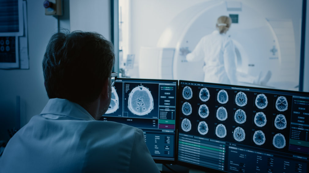 In Medical Laboratory Patient Undergoes MRI or CT Scan Process under Supervision of Radiologist, in Control Room Doctor Watches Procedure and Monitors with Brain Scans Results.