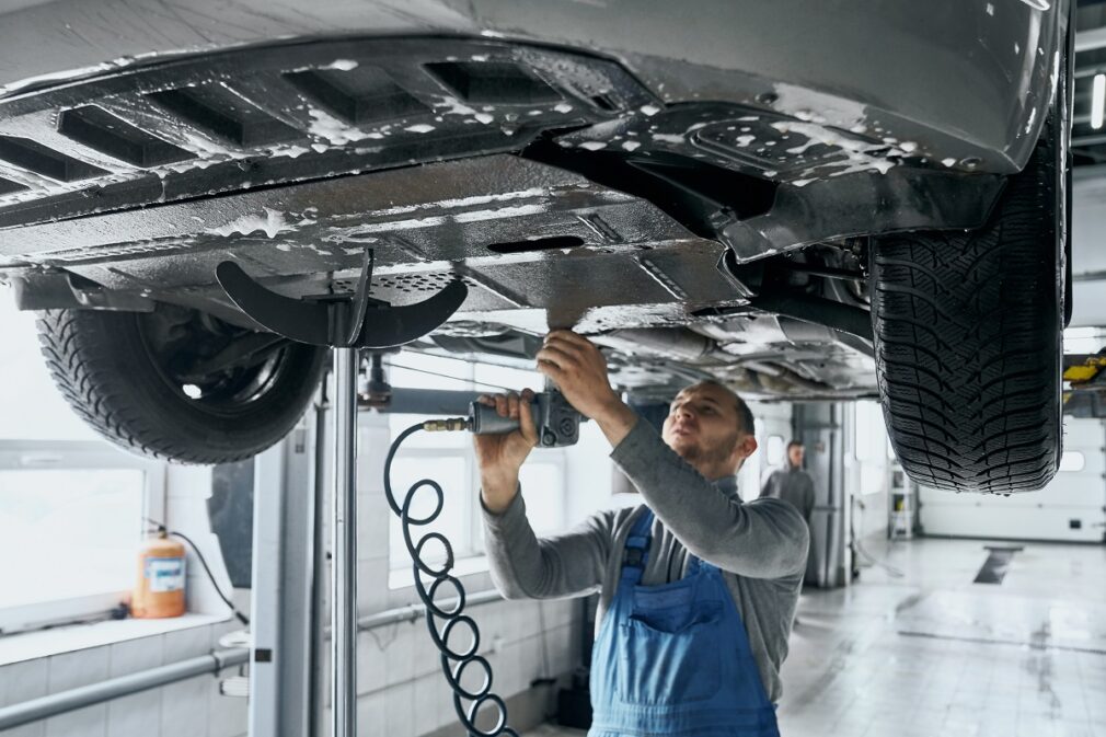 Competent mechanic in blue overalls repairing car suspension